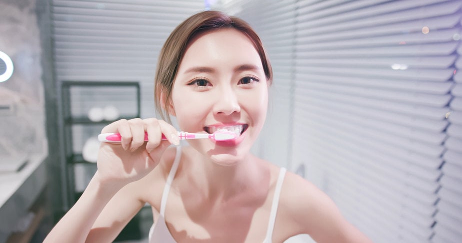ผู้หญิงยืนแปรงฟันให้สะอาดอยู่หน้ากระจก